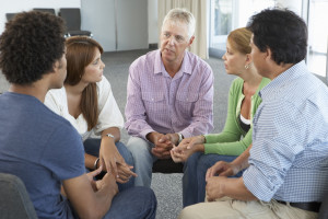 A group of conveniently diverse people sit in a circle during a support group session.