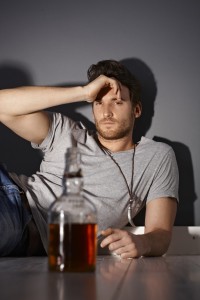 A depressed young man eyes a bottle of whiskey