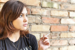 Teenager smokes by brick wall.