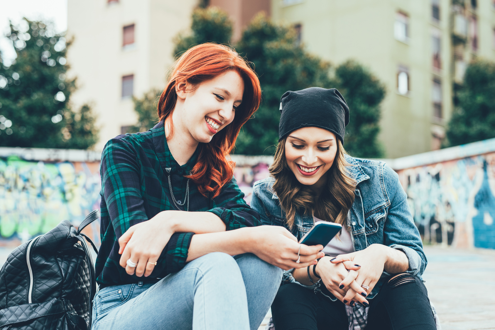 Girls outside looking at phone and laughing together. 