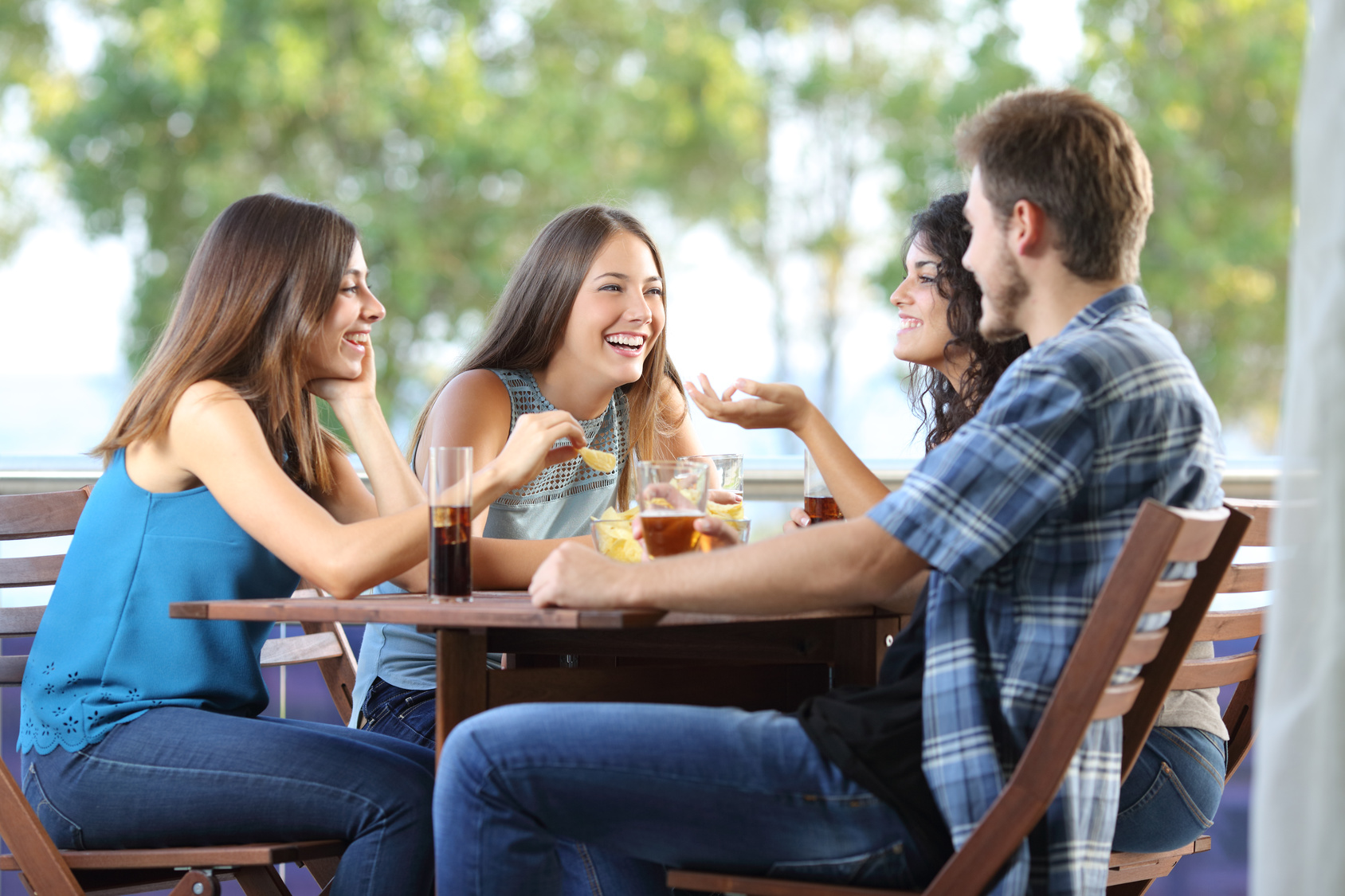 Group of young men and women talking outdoors at a table with drinks
