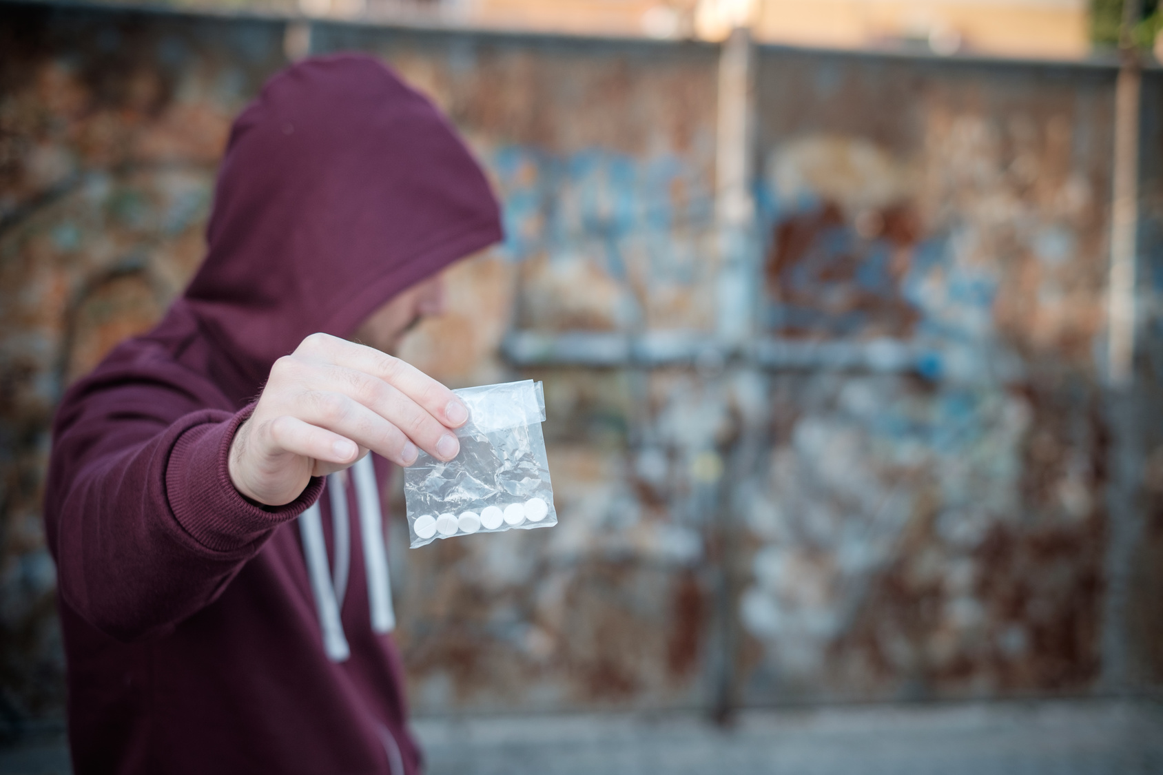 A man in a red hoodie sells some drugs. He's white.