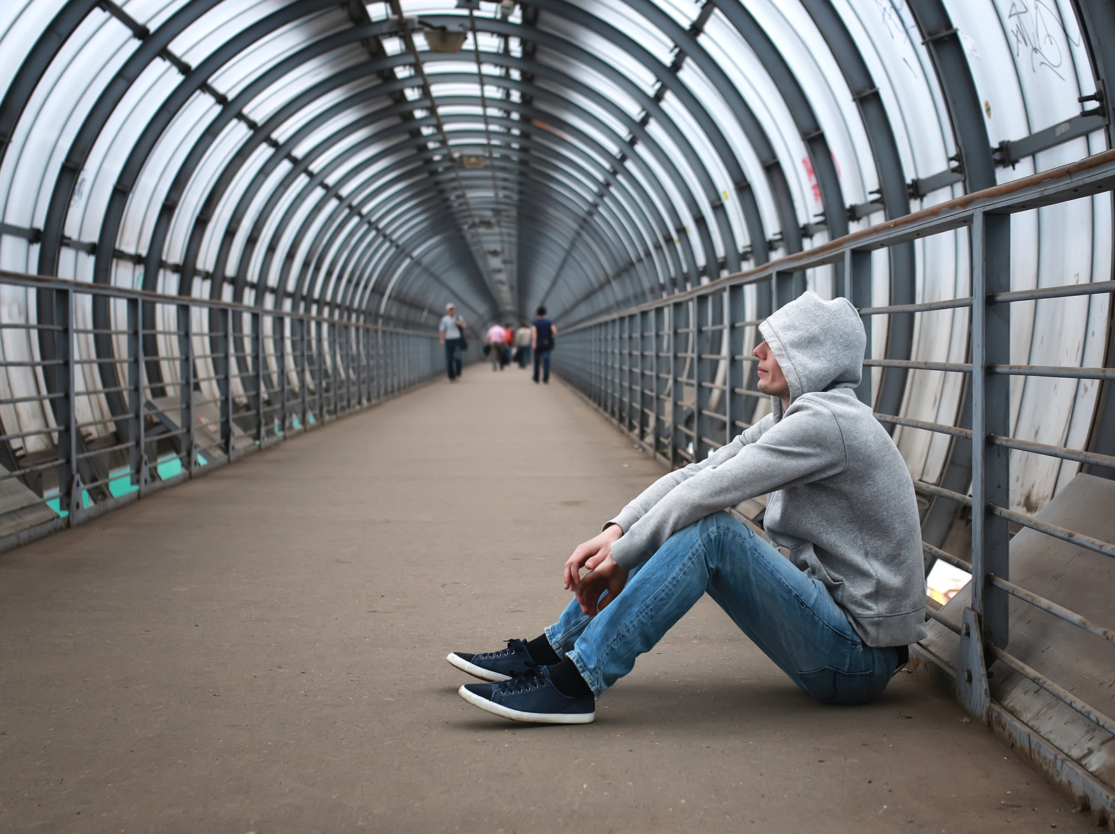 A man in a grey hoodie sits on the ground, waiting to deal drugs.